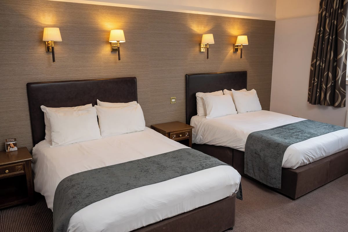 A hotel room with two beds, each with a headboard, bedside tables, and lamps.