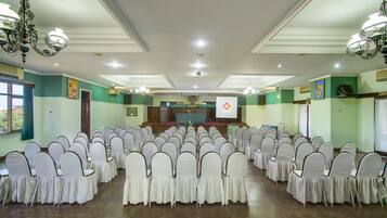 A conference room with rows of white chairs, a stage with a podium, and chandeliers.