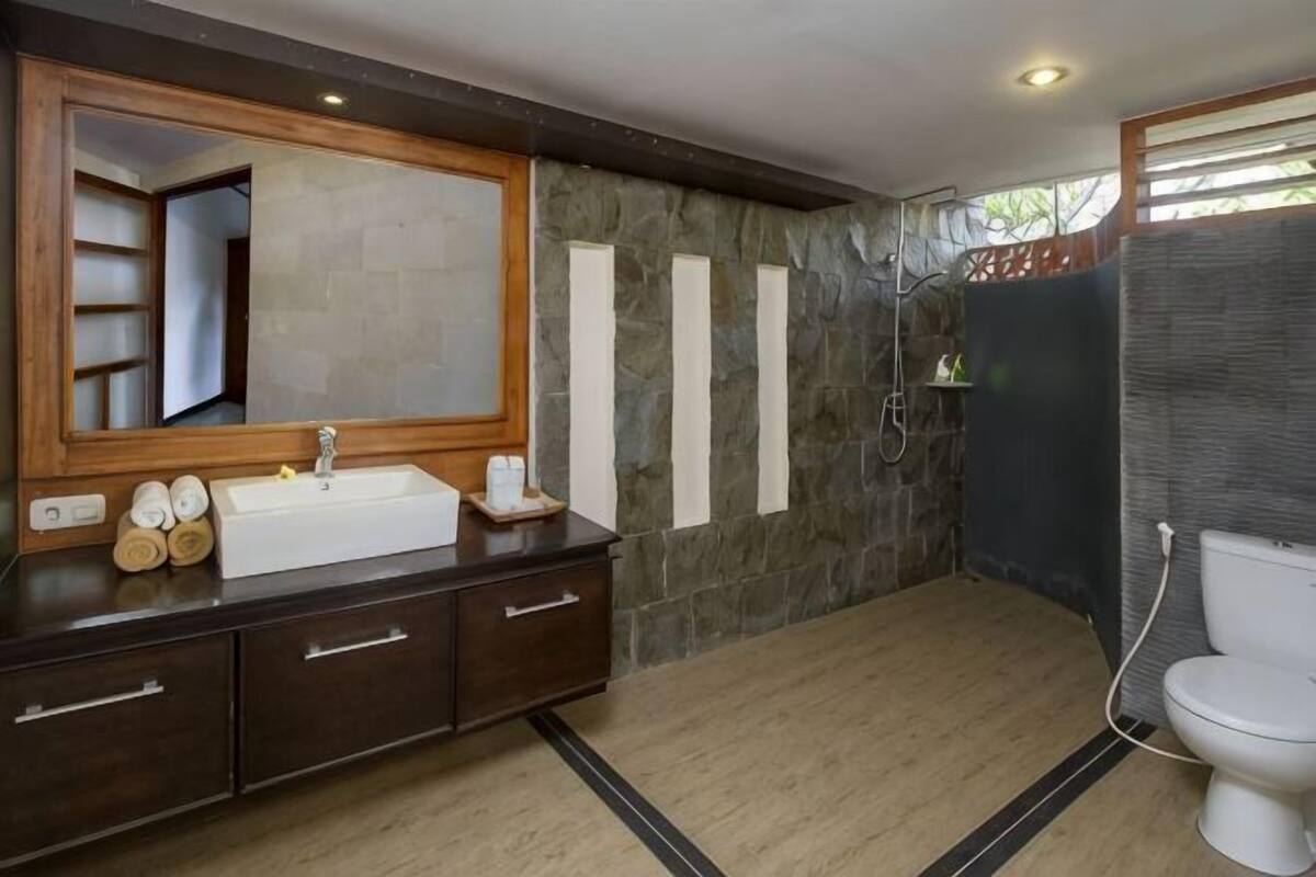 Une salle de bain avec un grand miroir, un lavabo, des toilettes et un espace douche.