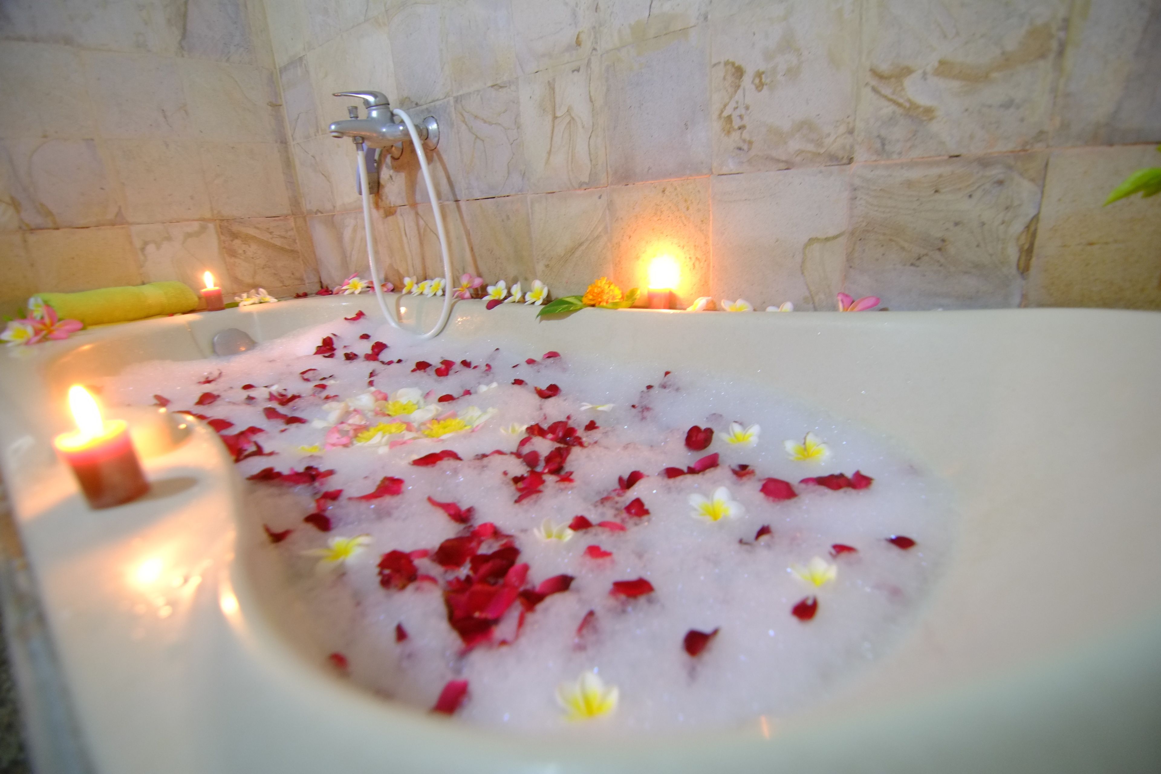 Een bad vol water, rozenblaadjes en kaarsen, doet denken aan een spa.