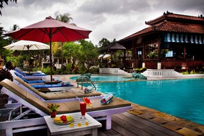 Un espace aménagé au bord de la piscine, avec des chaises longues, des parasols et une table où sont disposés des fruits et une boisson.