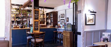 A bar area with wooden stools, shelves of bottles, and a chalkboard menu.