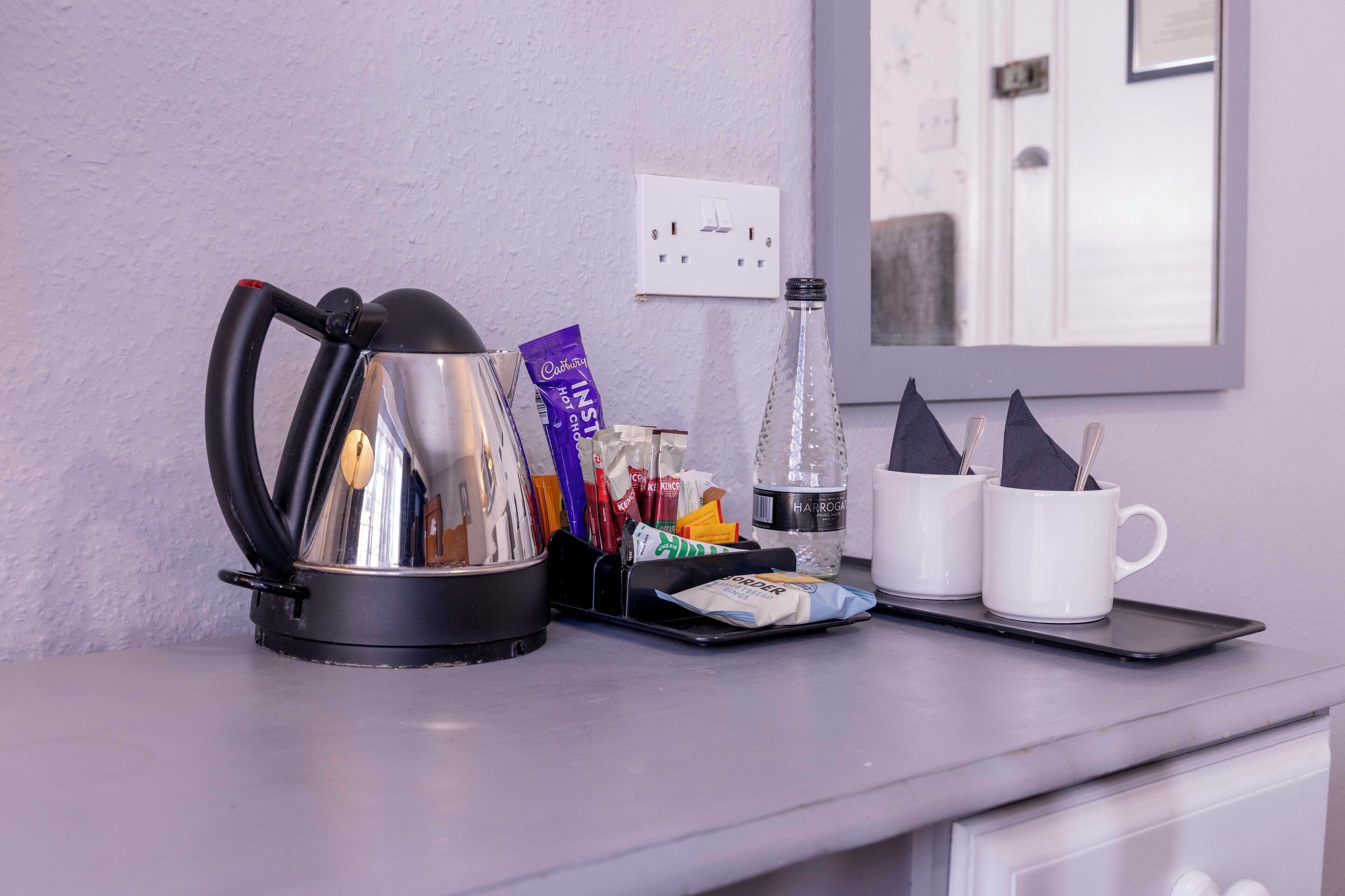 A kitchen counter with a kettle, a tray with coffee cups and sugar packets, a bottle of water, and a coffee machine.