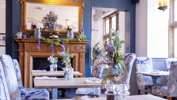 A dining area with tables set for two, featuring floral centerpieces and salt and pepper shakers.