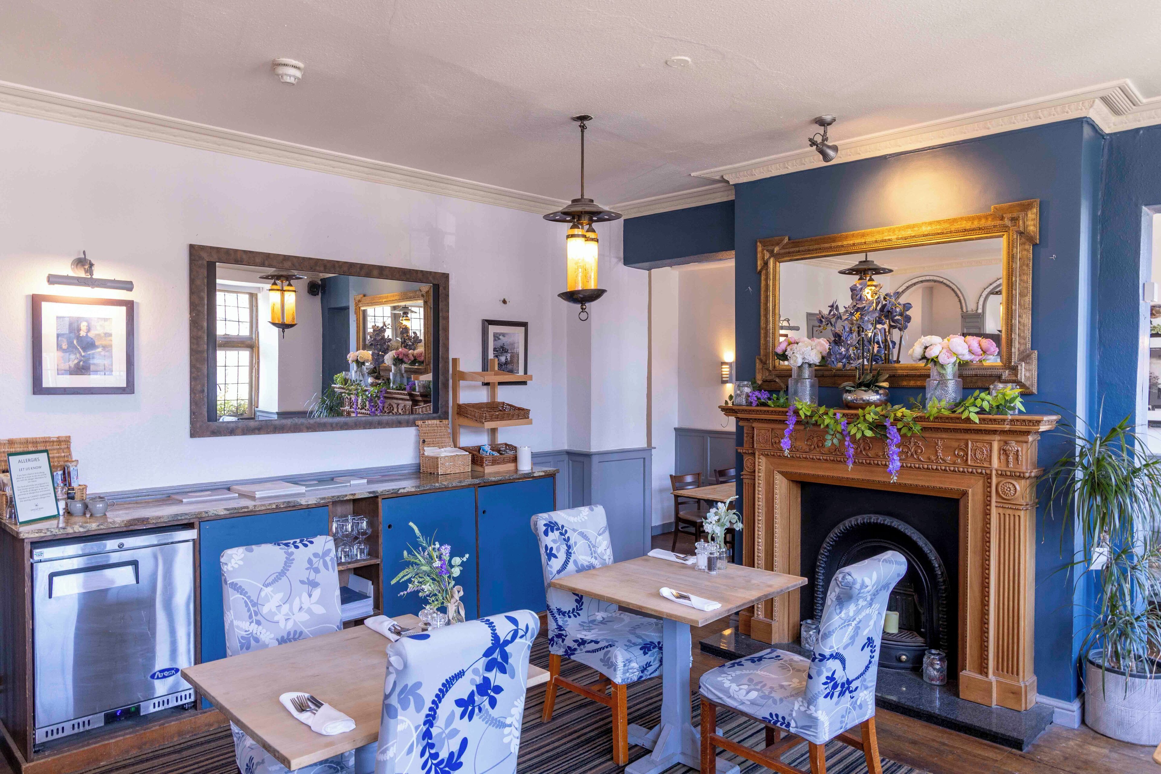A dining area with blue and white patterned chairs, a wooden table, a fireplace with a mirror above, and a ceiling light fixture.