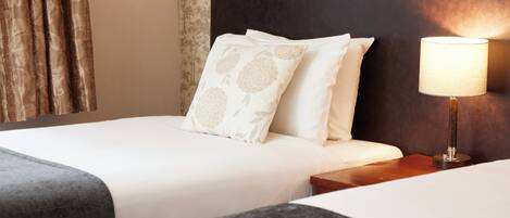A hotel room with a bed, pillows, a nightstand, and a lamp.