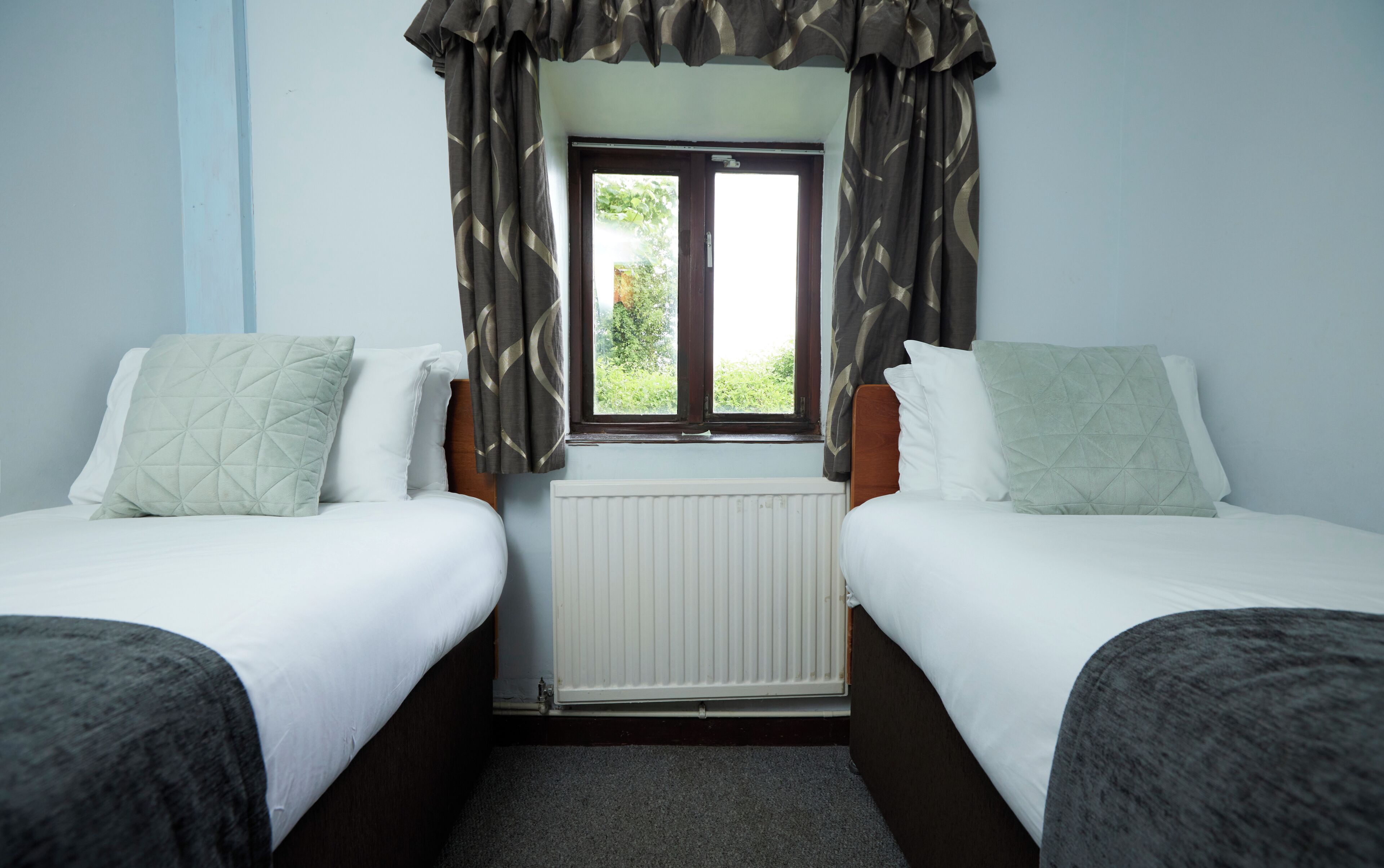 A twin room with two beds, a window with curtains, and a radiator.