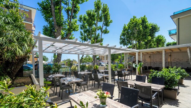 Un espace extérieur aménagé en terrasse, avec des tables et des chaises, entouré de plantes en pot et d’arbres.