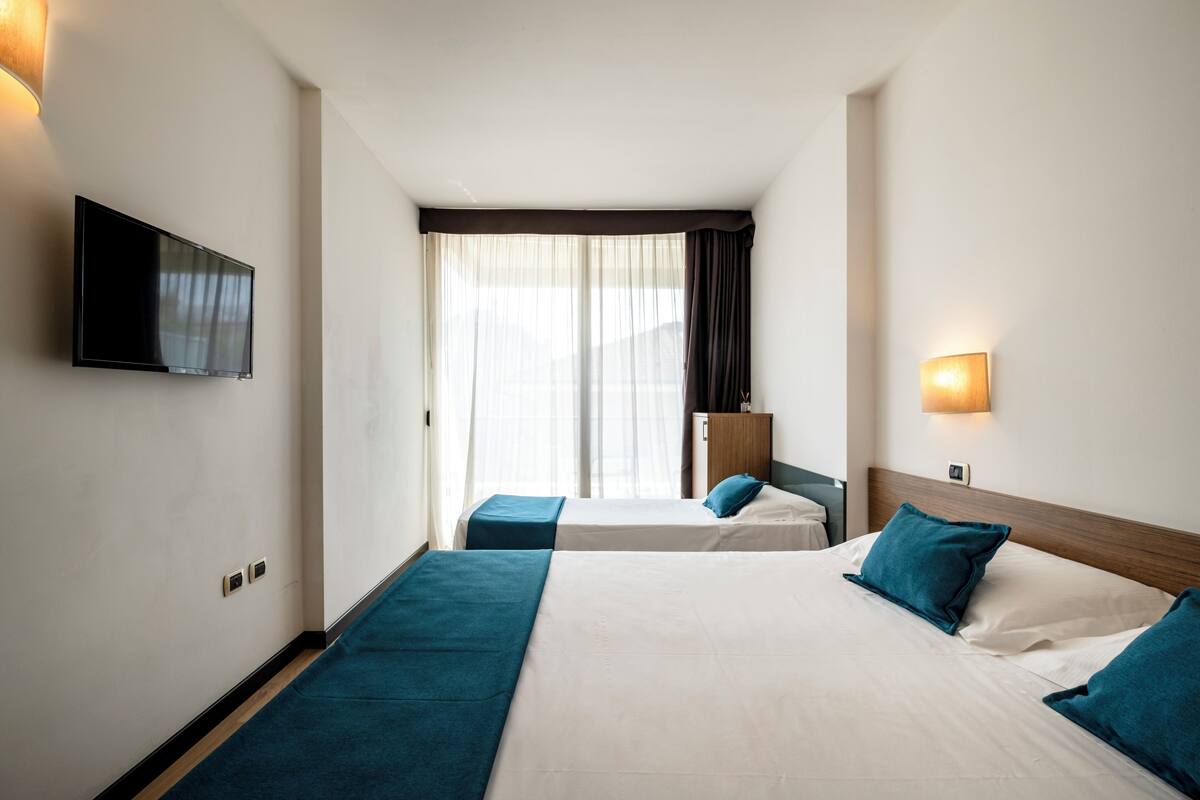 A hotel room with two beds, a TV, a desk, and a window with curtains.
