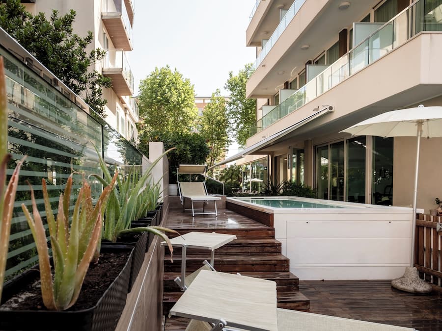 Un área de piscina moderna al aire libre con cubierta de madera, sillas de descanso y un jacuzzi.