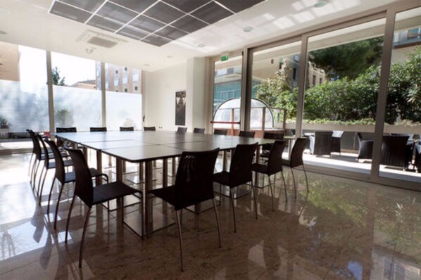 A conference room with a long table and chairs, large windows with a view of greenery and buildings, and a tiled ceiling. - Hotel Cristallo (Rimini)