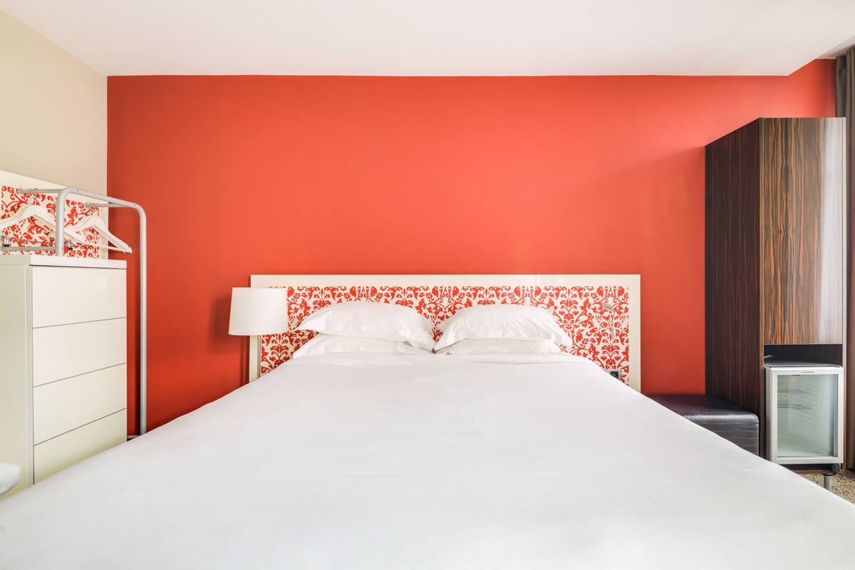 Une chambre d’hôtel avec un grand lit, une table de chevet, une commode et un petit réfrigérateur.