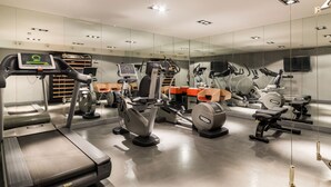 Un gimnasio moderno con varios equipos de ejercicio, una pantalla digital y un espejo grande.