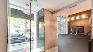 Un área de recepción moderna con un puerta de vidrio que da a la calle, un mostrador de recepción y una lámpara decorativa.