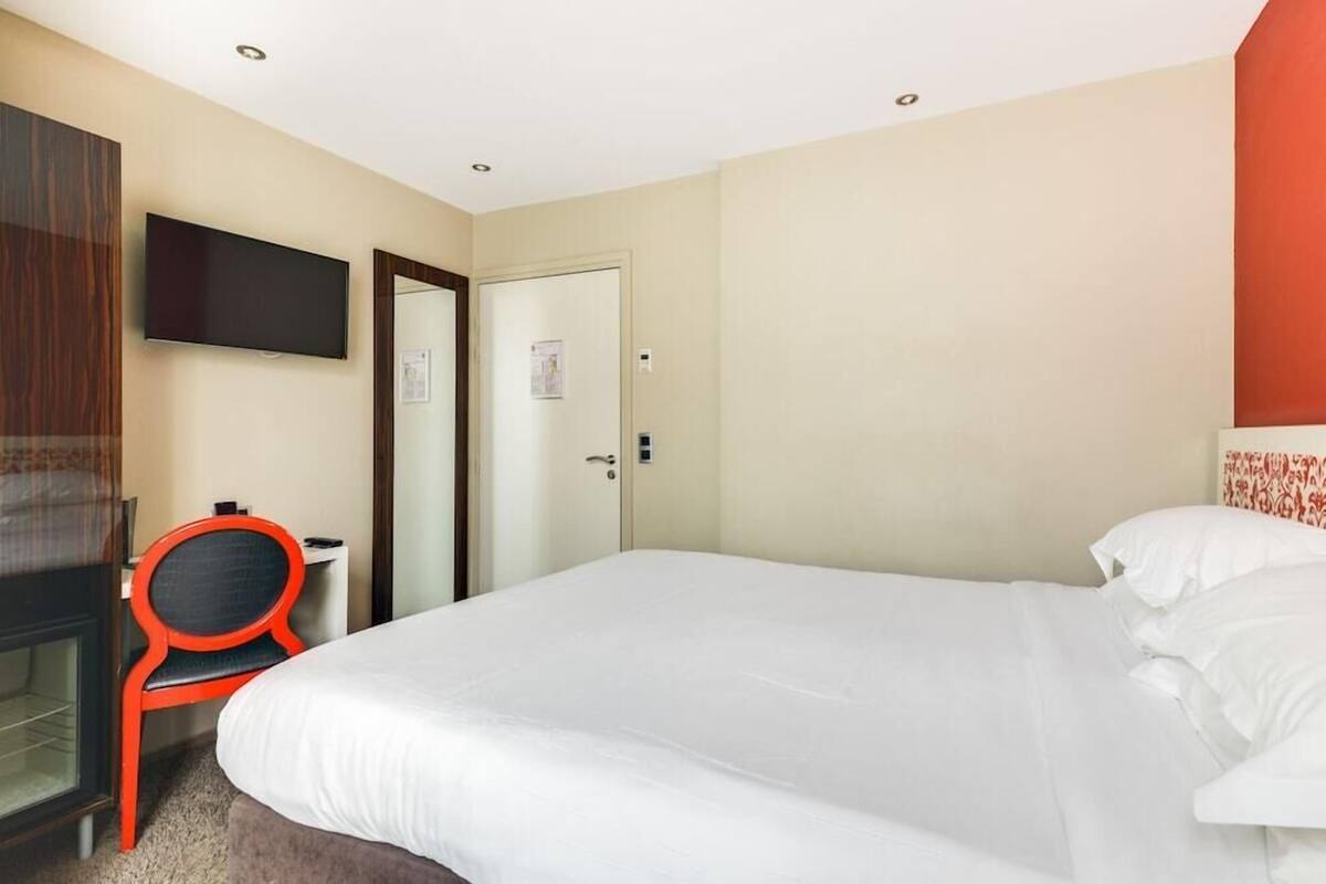 Une chambre d’hôtel avec un lit, un téléviseur fixé au mur, un bureau avec une chaise et une porte.