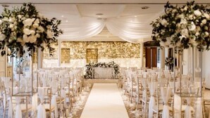 Une allée où se déroule la cérémonie de mariage, avec des chaises blanches et des décorations florales.