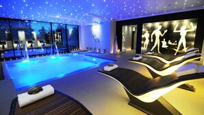 Un spa moderne doté d’une grande piscine intérieure, d’espaces de détente et d’un mur orné de silhouettes de personnes.