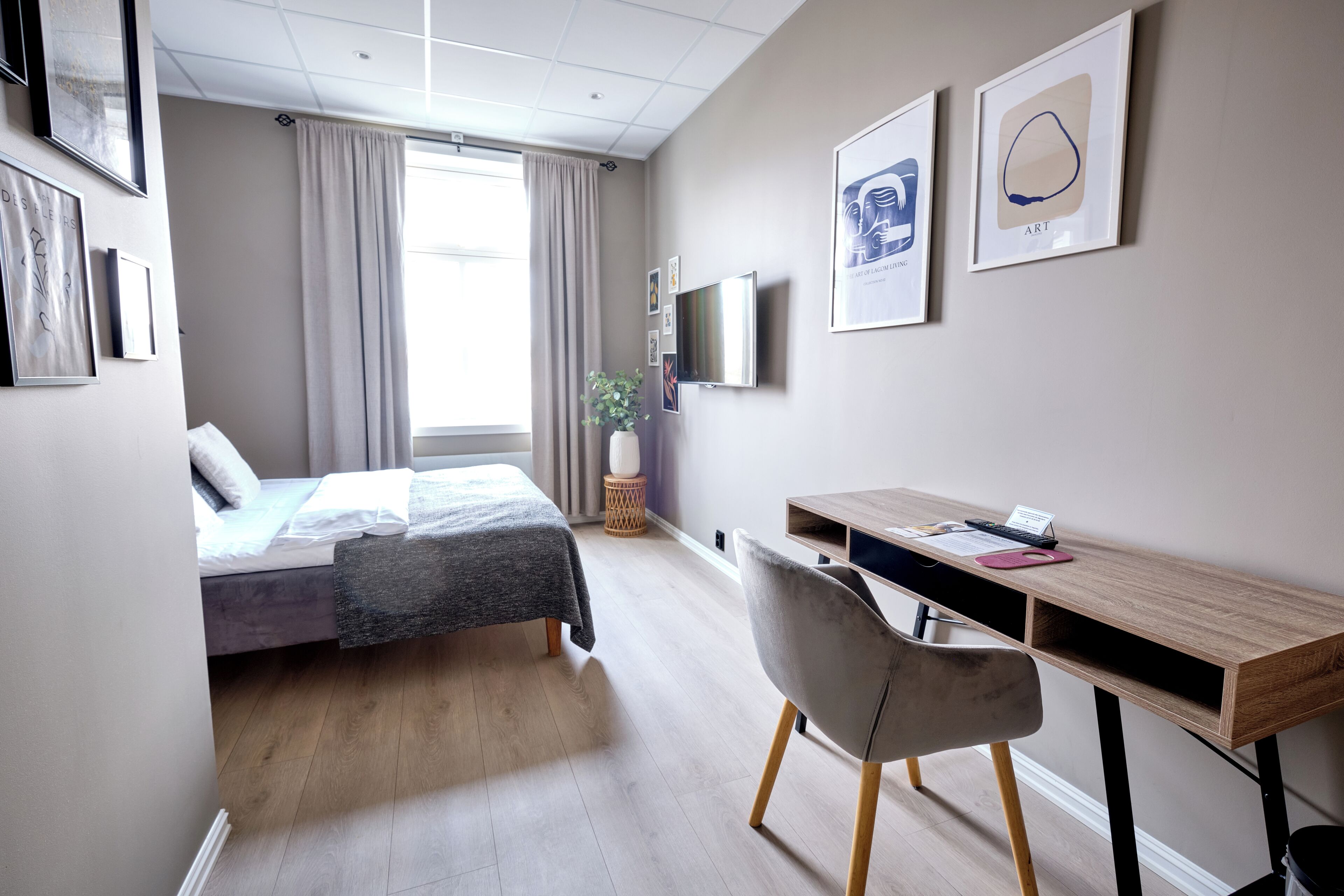 Een moderne hotelkamer met een bed, bureau, stoel, televisie en kunst aan de muur.