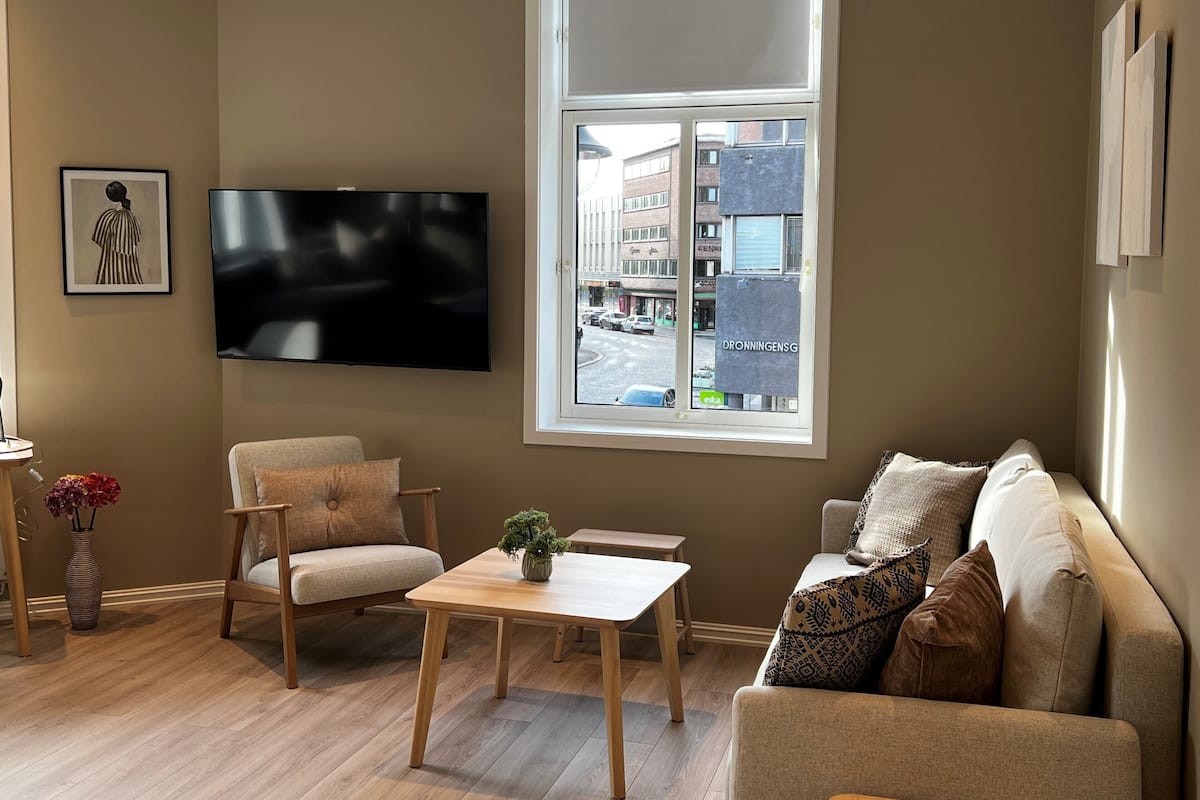 Una sala de estar con un ventanal grande, un televisor de pantalla plana, un sofá, una mesa de centro y un sillón.