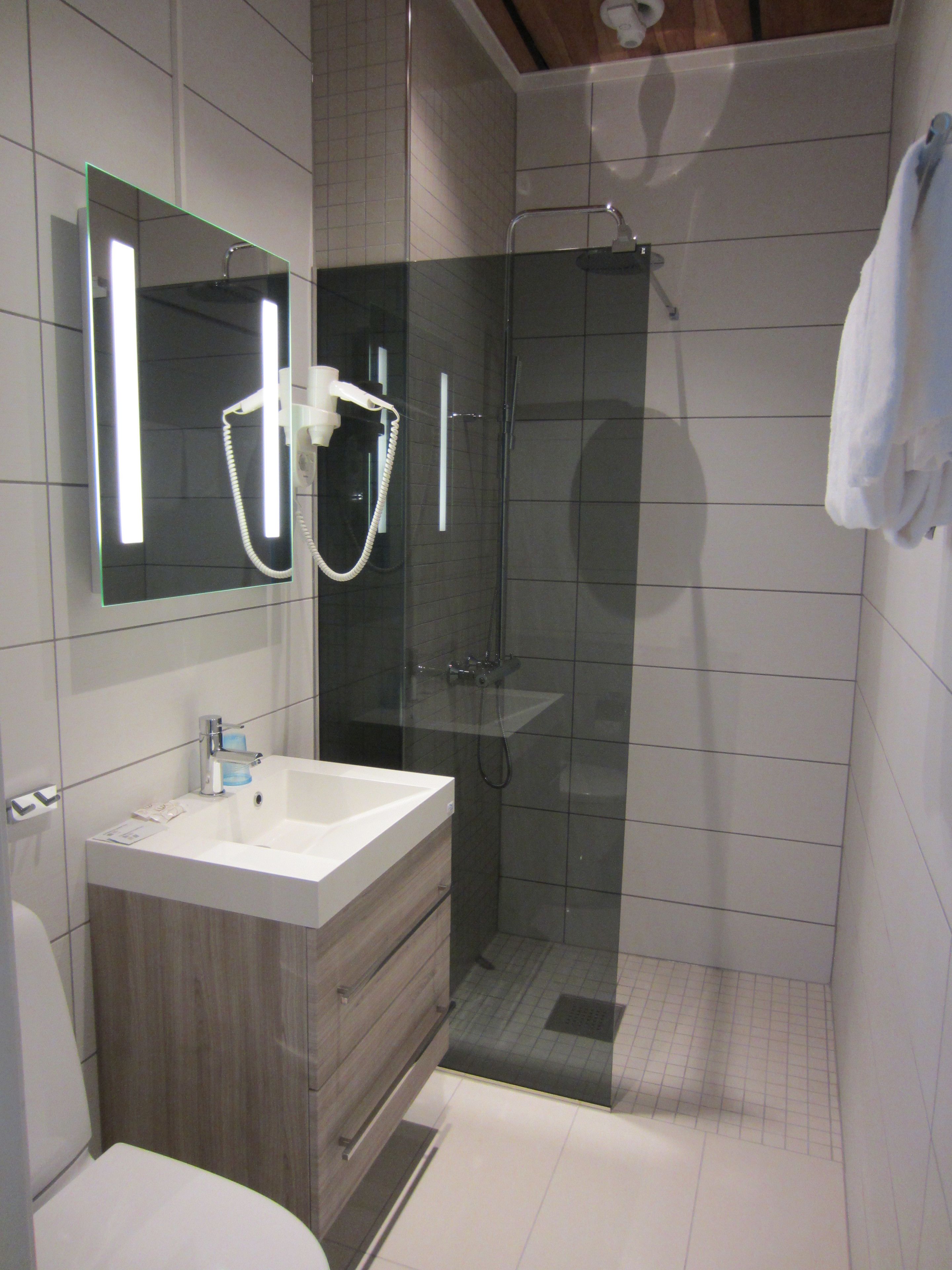 Un baño moderno con ducha envuelta en vidrio, un lavamanos blanco y un espejo sobre él.