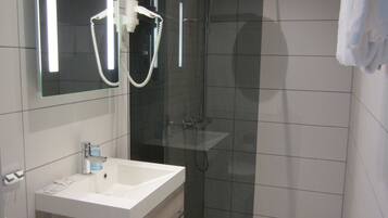 Un baño moderno con ducha envuelta en vidrio, un lavamanos blanco y un espejo sobre él.