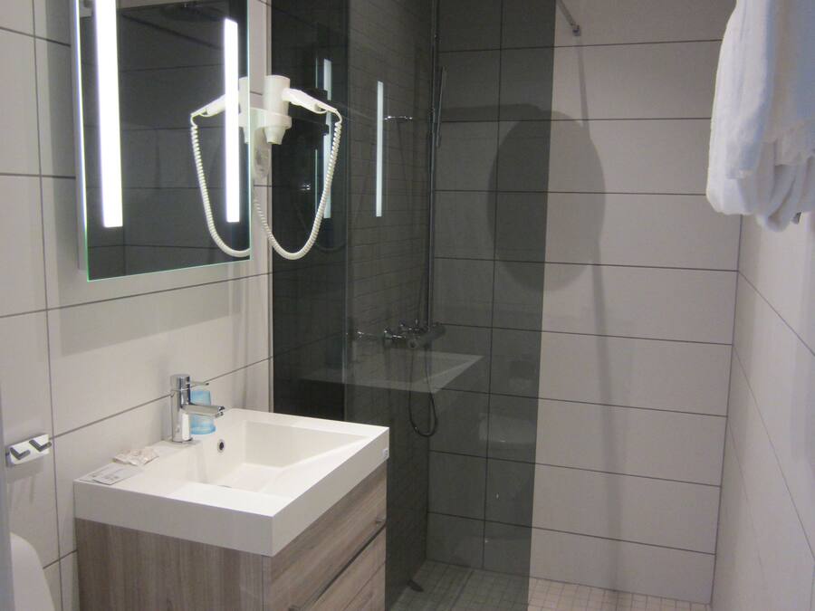 Un baño moderno con ducha envuelta en vidrio, un lavamanos blanco y un espejo sobre él.