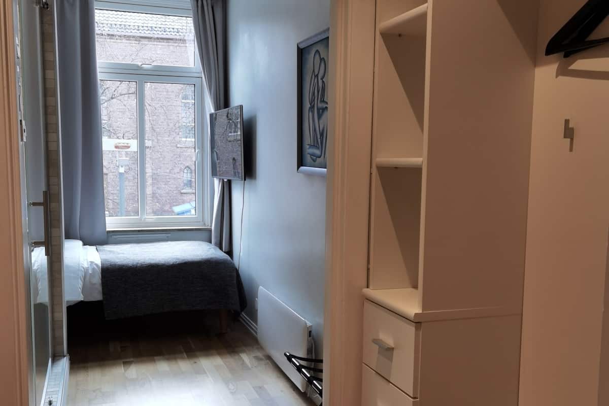 Un dormitorio con cama, radiador, armario y ventana con cortinas.
