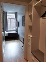 Un dormitorio con cama, radiador, armario y ventana con cortinas.