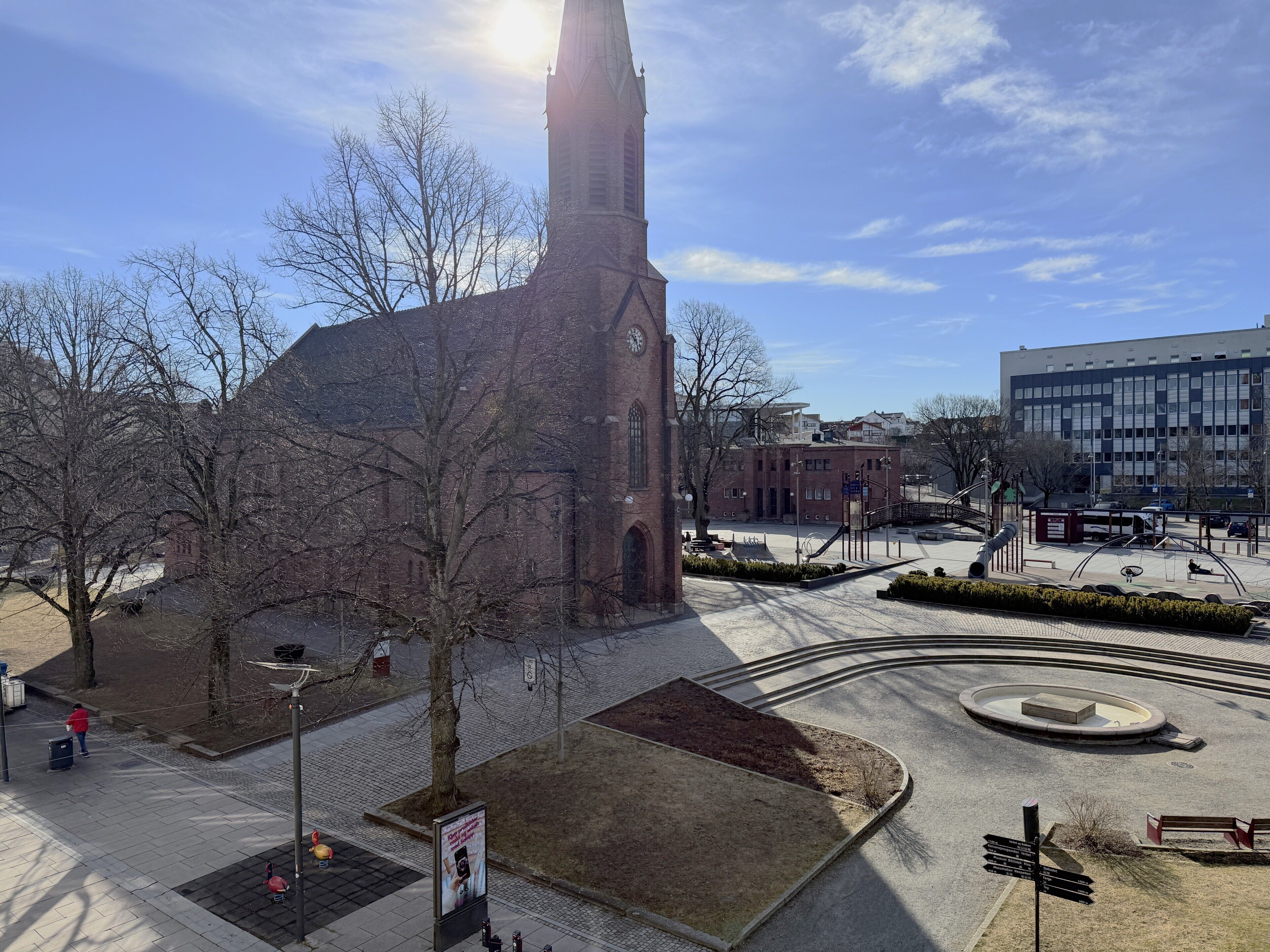 A church with a tall steeple, a modern building, and a circular plaza with benches.