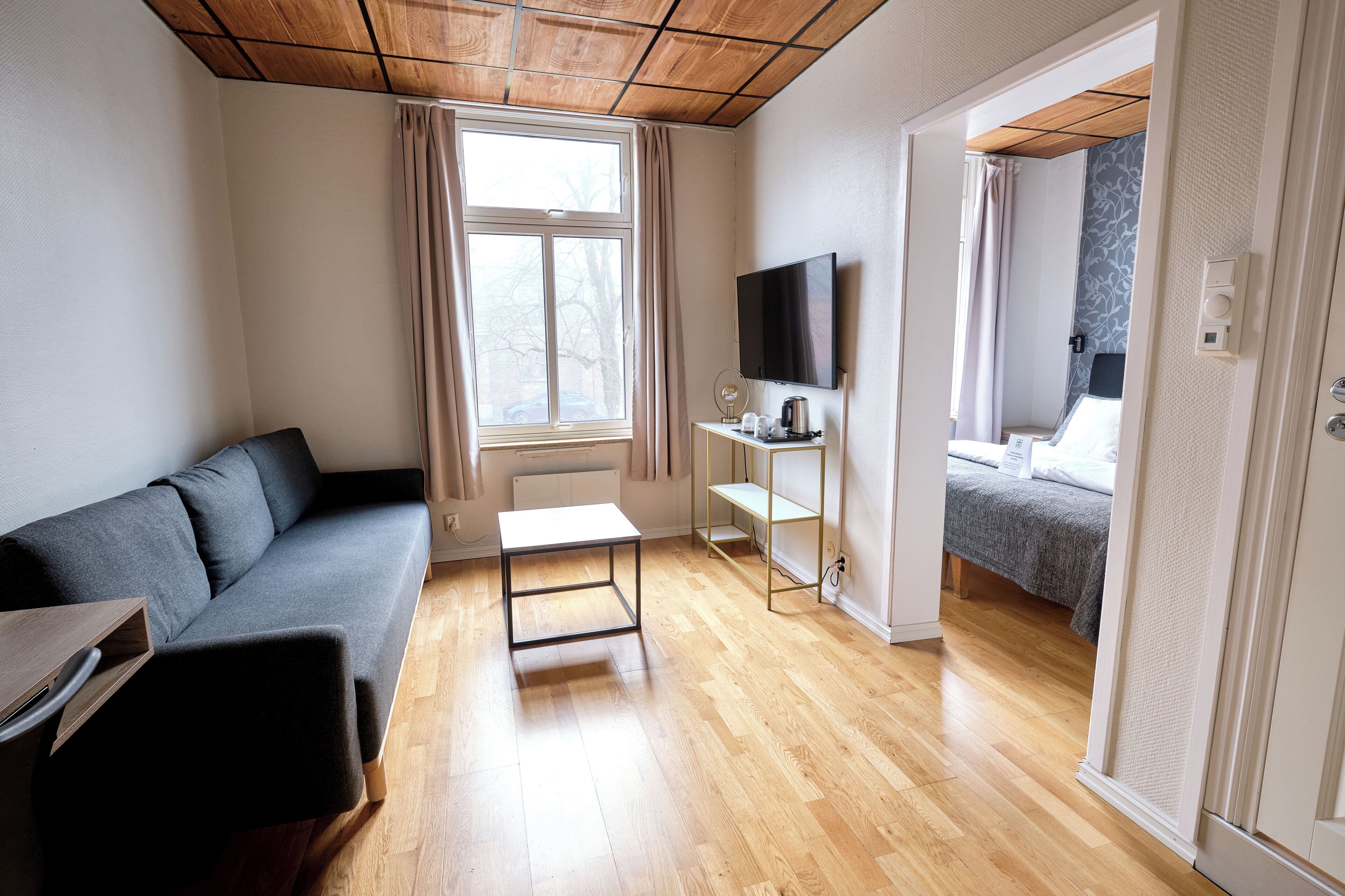A modern room with a sofa, a small table, a TV, and a bed with a patterned wall.