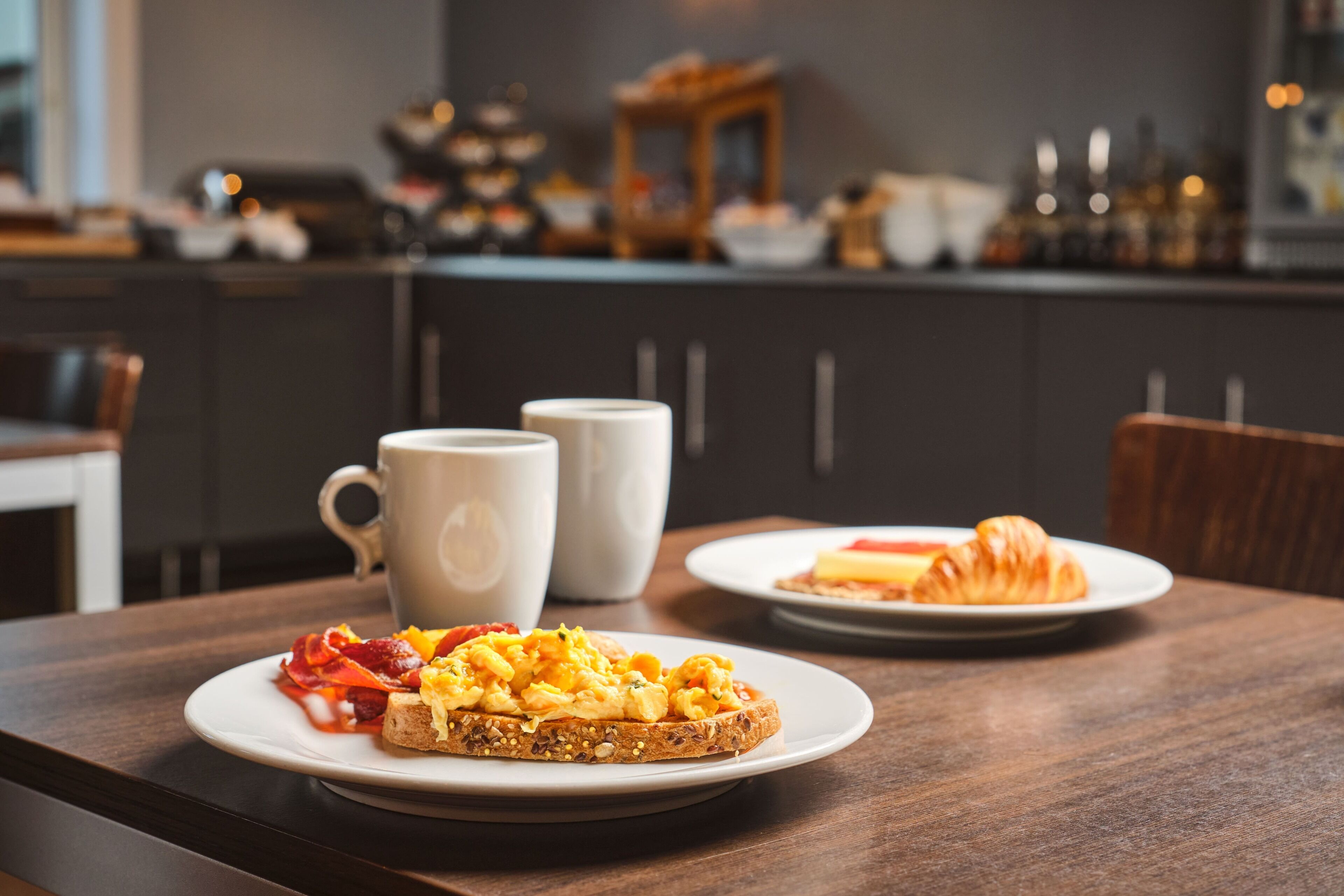 A breakfast setting with toast, scrambled eggs, and a croissant on a wooden table.