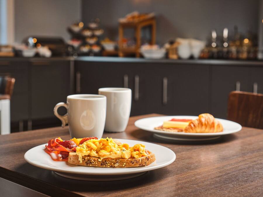 A breakfast setting with toast, scrambled eggs, and a croissant on a wooden table.