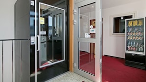 Entrada de hotel con puerta de vidrio, máquina expendedora y alfombra roja.