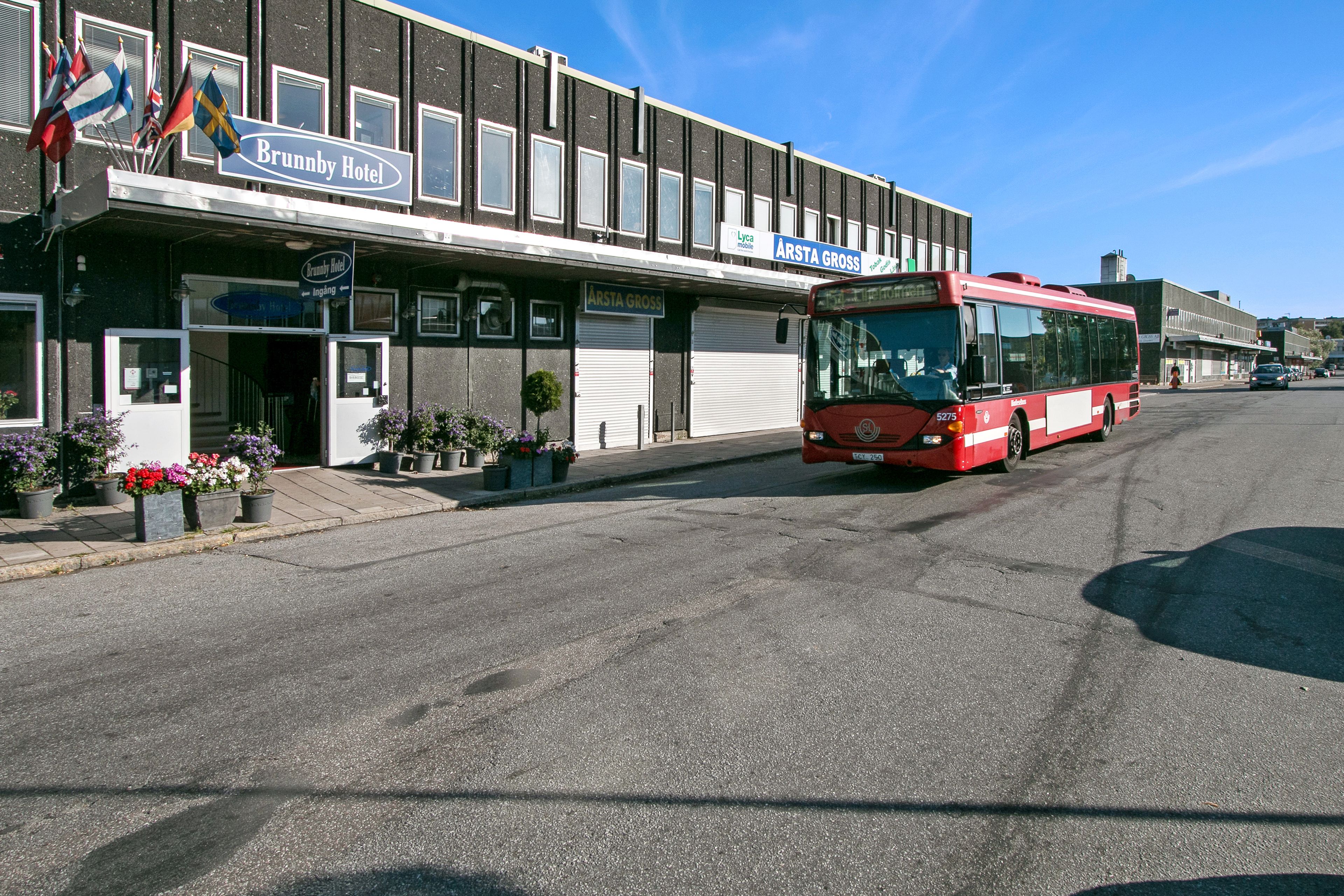 A red bus parked in front of a hotel with a sign reading "Brunnby Hotel".
