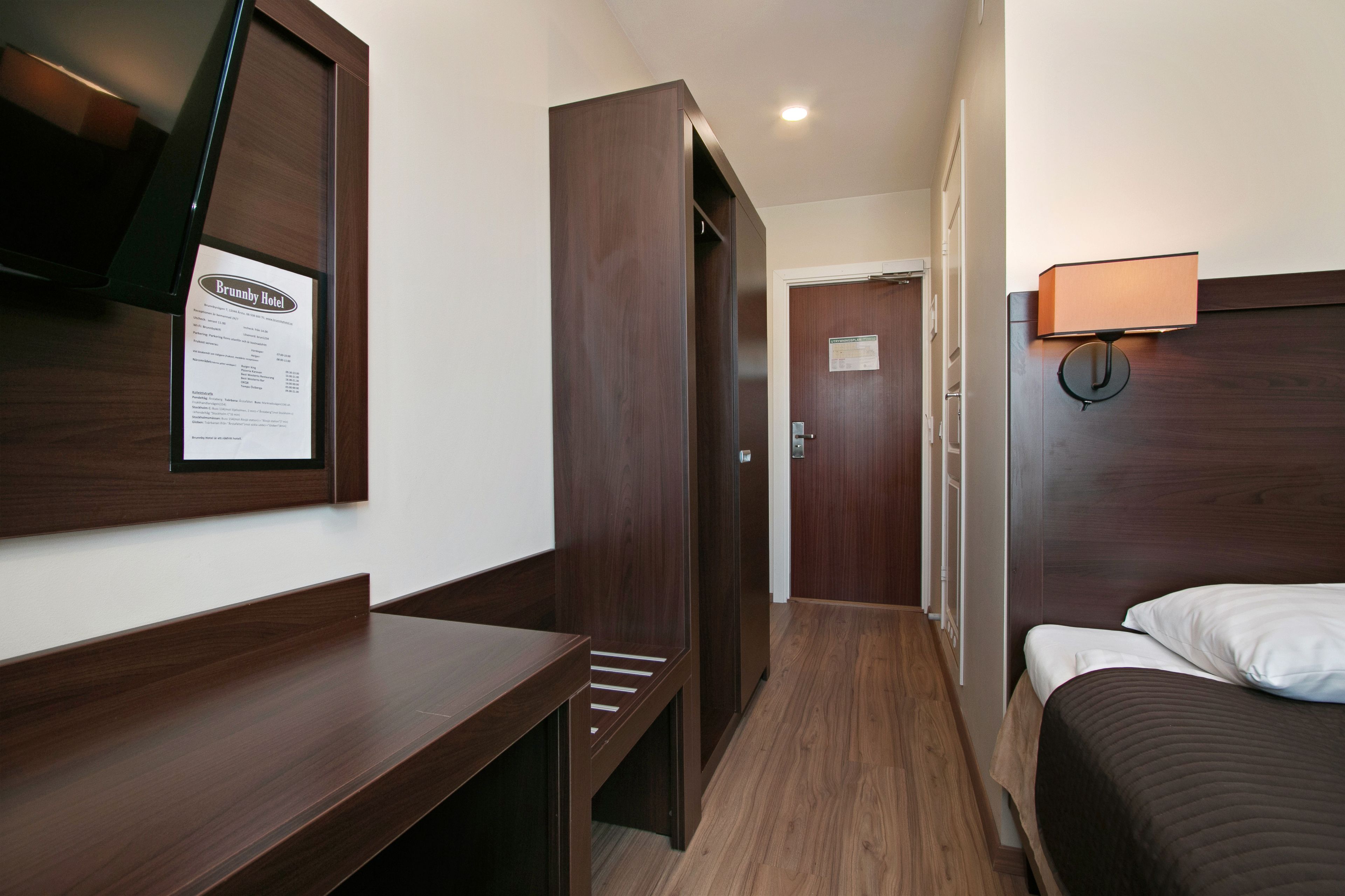 Ein Hotelzimmer mit einem Holztisch, einem Bett, einer Wandlampe und einer Tür zu einem weiteren Raum.
