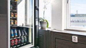 Una máquina expendedora con bebidas, una planta en maceta y una ventana con vistas.