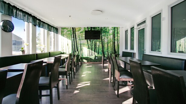 Un restaurante con una barra alargada, cabinas y un amplio ventanal con vistas a árboles.