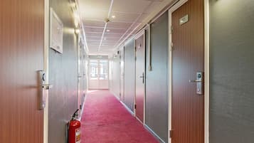 Corridoio di un albergo con tappeto rosso, porte in legno e un estintore.