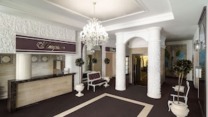 A reception area with a marble counter, a chandelier, and a bench. - Flowers Hotel (Chisinau)