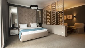 A modern hotel room with a large bed, a desk with a chair, a sofa, a large mirror, and a decorative partition. - Flowers Hotel (Chisinau)