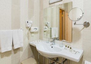Une salle de bain moderne avec un lavabo blanc, deux sèche-cheveux, un porte-serviettes et un grand miroir.