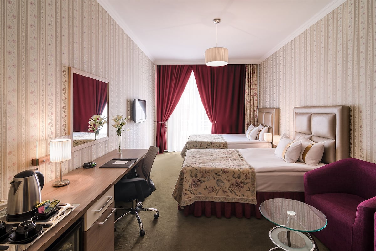Habitación de hotel con escritorio, dos camas, una silla, una mesita y un espejo.