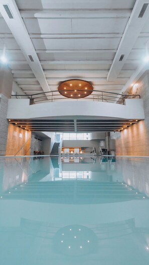 An indoor swimming pool with a central circular light fixture, a staircase leading to a mezzanine, and a view of the pool's edge. - Hotel Spa Republica (Mar del Plata)