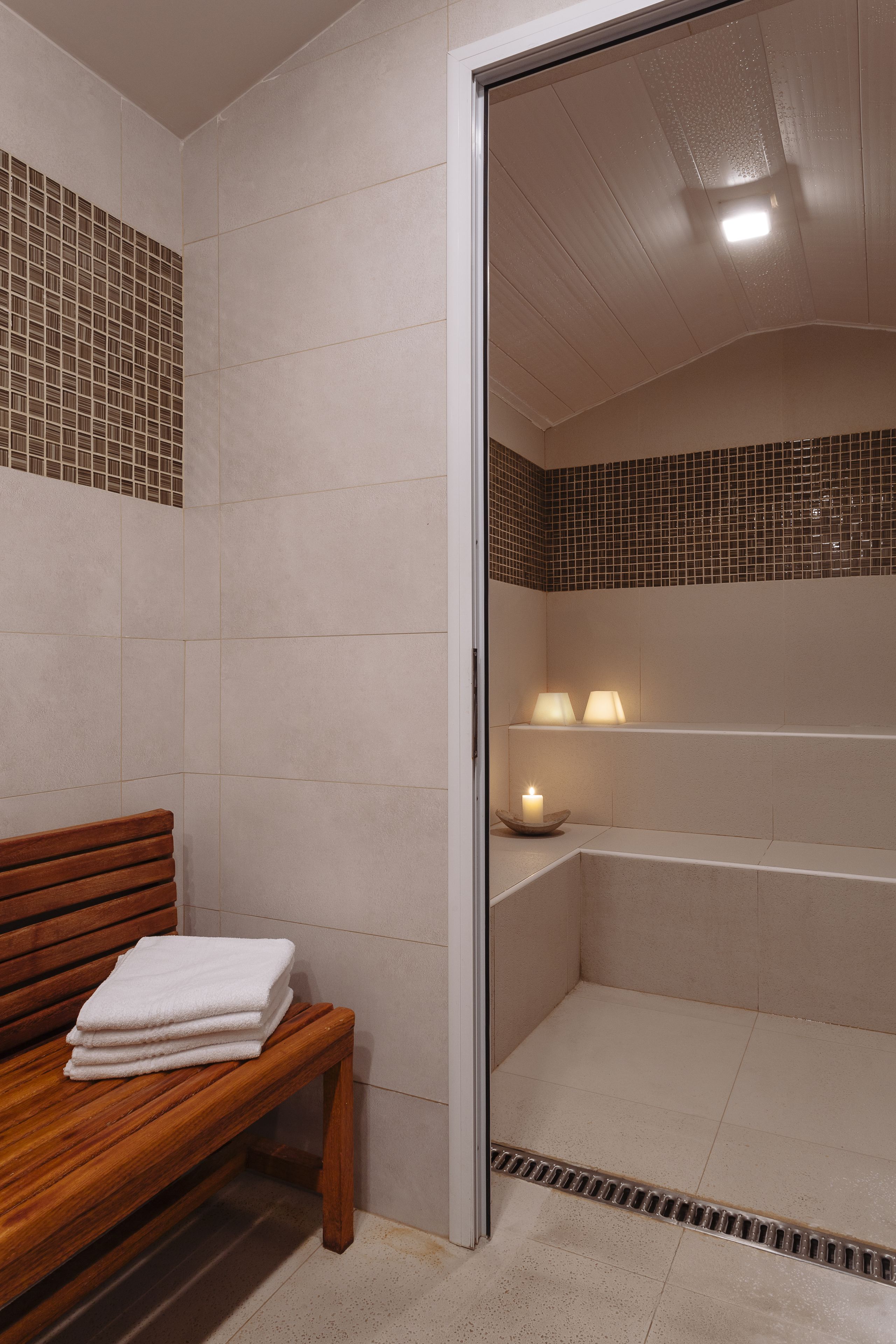 A bathroom with a wooden bench, a bathtub, and two wall-mounted lamps.