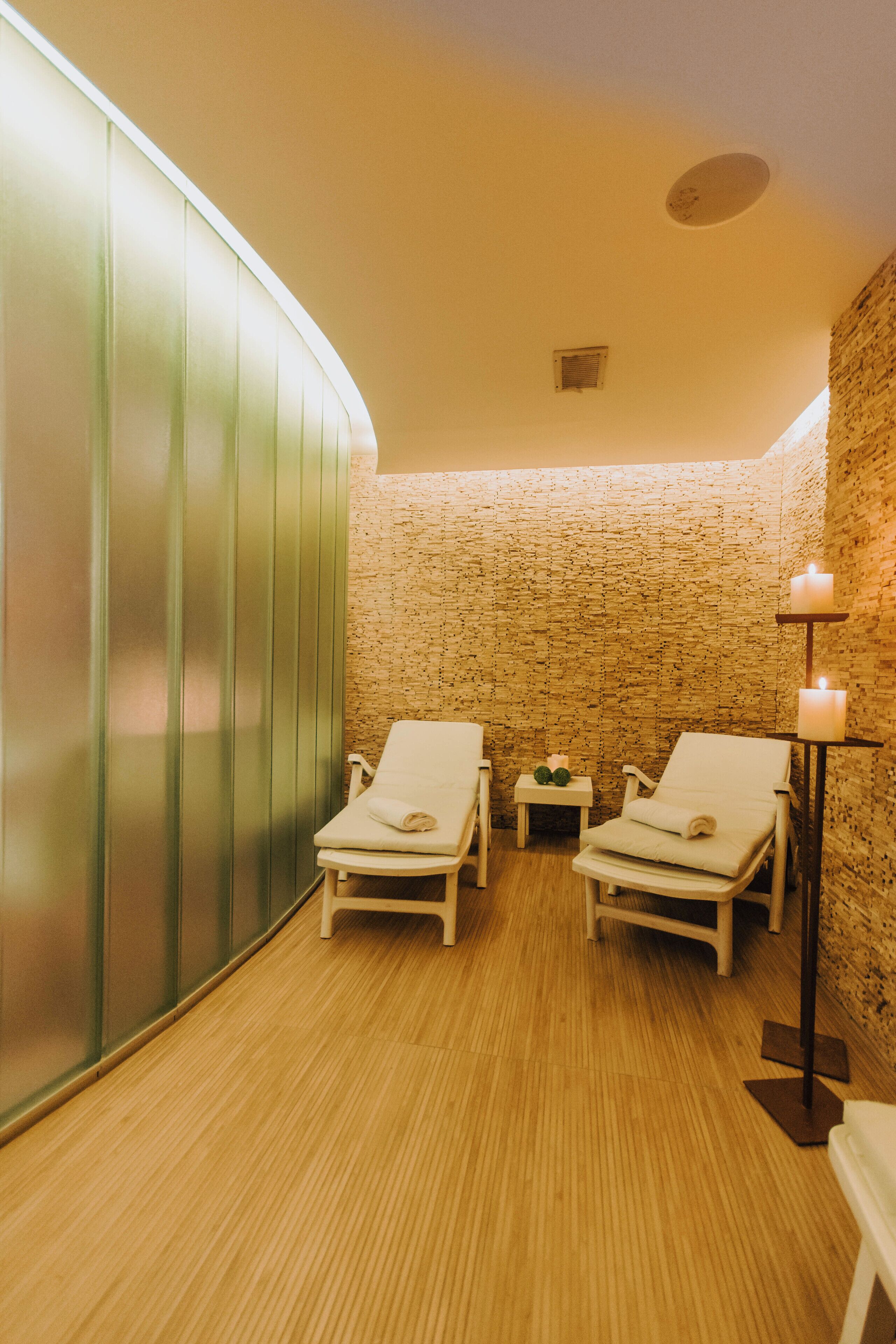 Une salle de spa avec deux fauteuils blancs, une petite table avec une bougie et un mur en briques.