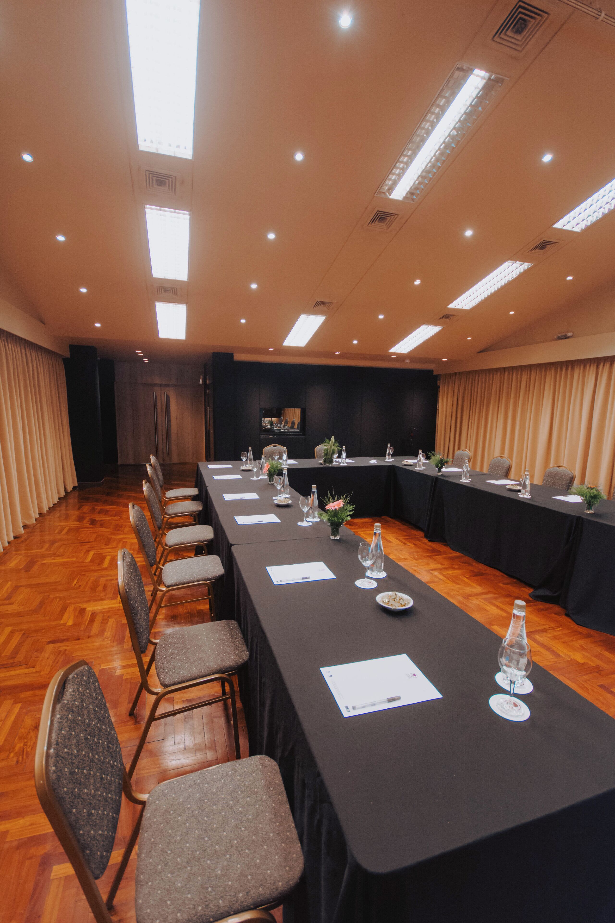 Un salón de conferencias con una larga mesa, sillas y un área para presentaciones.