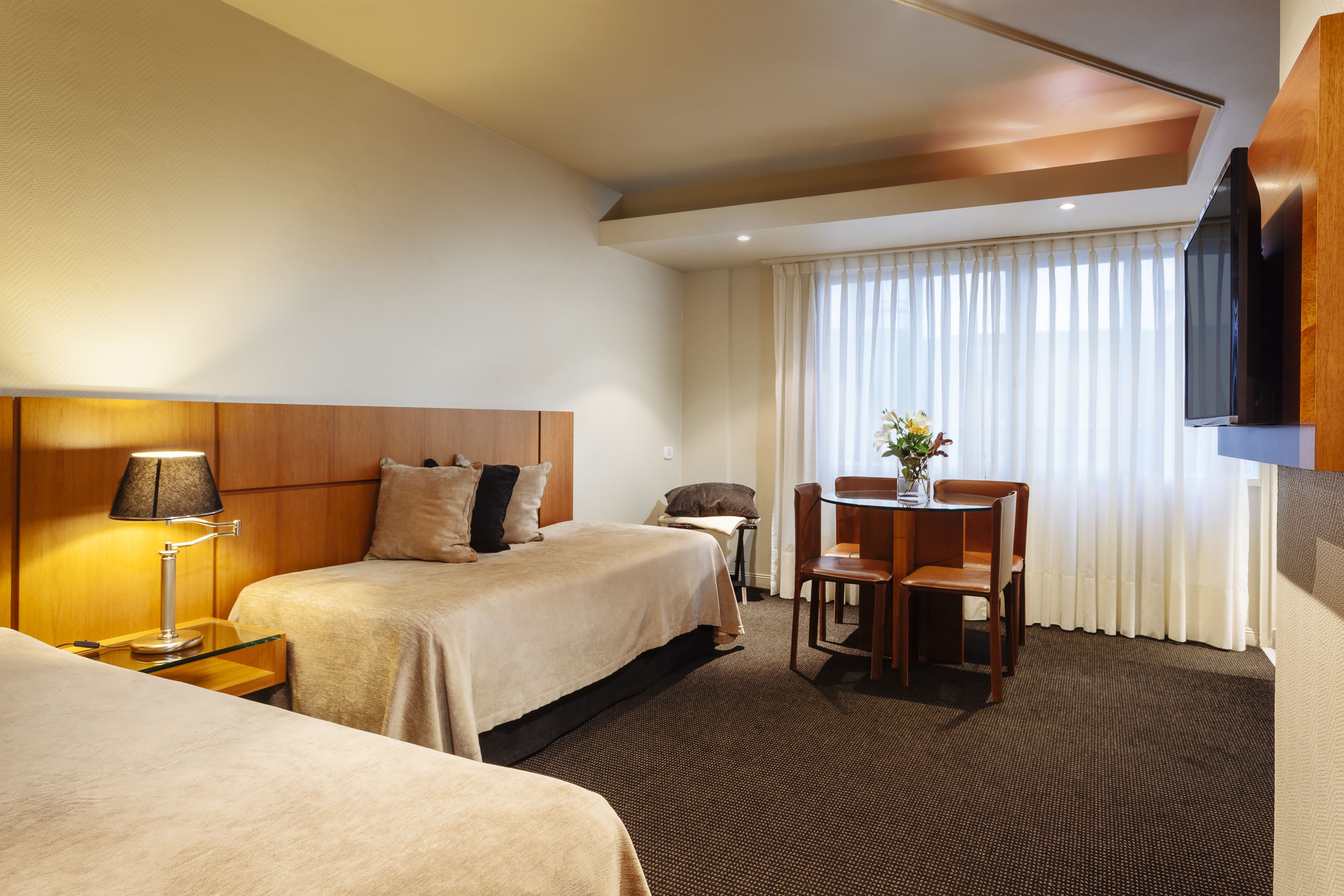 Une chambre d’hôtel avec deux lits, un bureau, une chaise, une télévision et une fenêtre avec des rideaux.