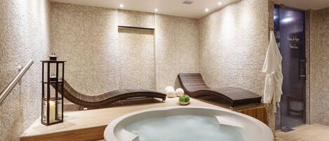 Un spa moderno con una bañera de hidromasaje, escalones de madera, una mesita con una vela y un perchero para toallas.