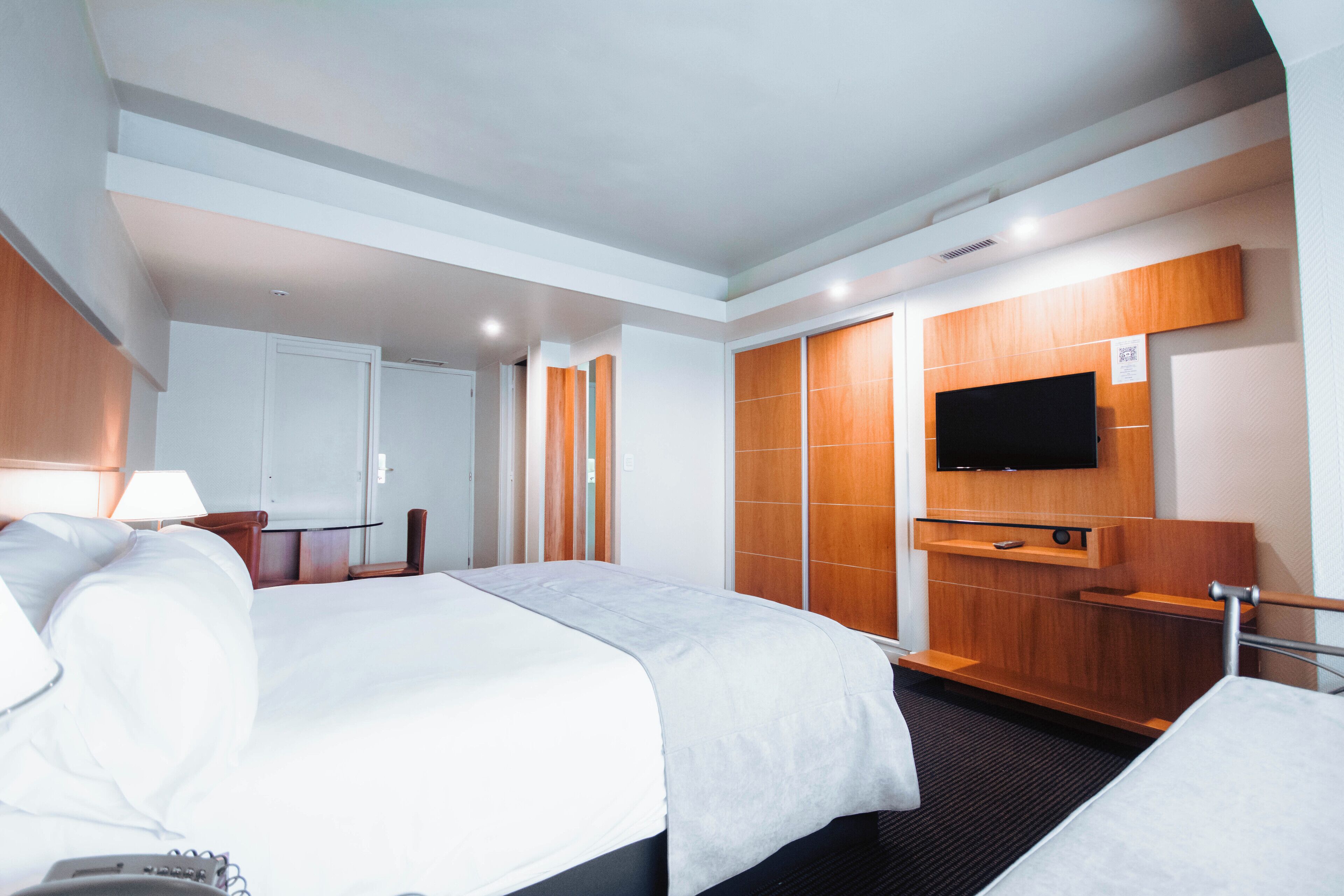 A hotel room with two beds, a TV mounted on the wall, and a wooden panel design.