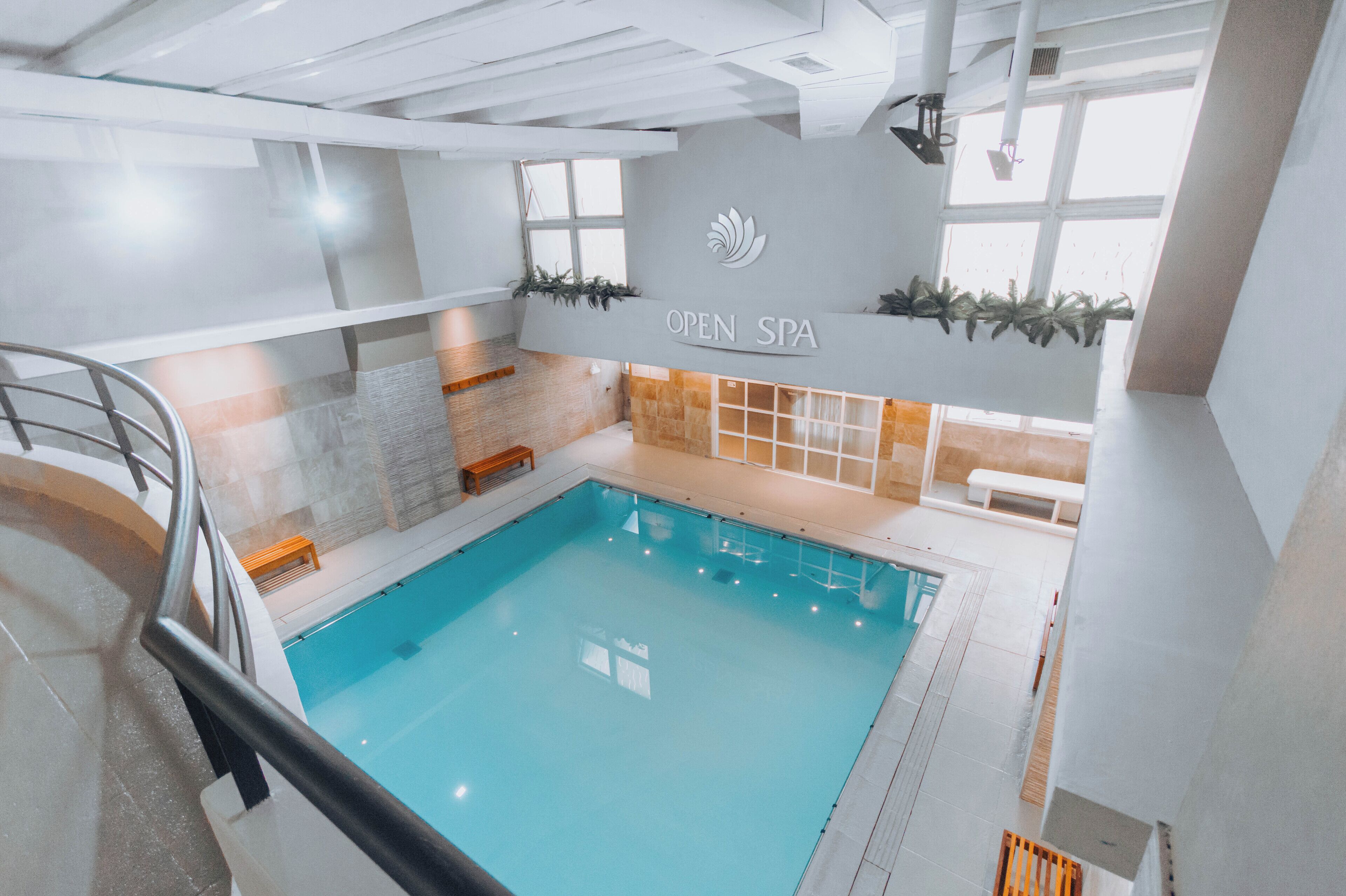 An indoor swimming pool with a reception area, a staircase, and a wall with a logo and text.